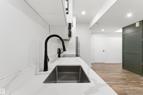 Kitchen featuring white cabinetry, a black gooseneck faucet, an undermount stainless steel sink, and light-toned countertops - 12447 47 Street, Edmonton, AB - Indoor Photo Showing Other Room