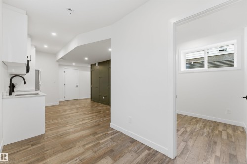 Contemporary interior featuring wood-finish flooring throughout, white cabinetry with a sink and matte black faucet, recessed lighting, and a feature wall with dark green paneling - 12447 47 Street, Edmonton, AB - Indoor Photo Showing Other Room