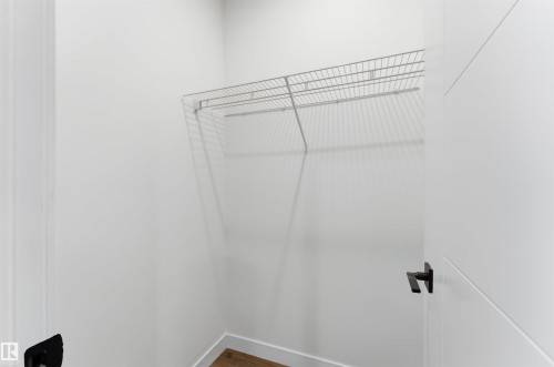 Walk-in closet featuring wire shelving, white walls, wood-finish flooring, and a modern white door with a matte black lever handle - 12447 47 Street, Edmonton, AB - Indoor With Storage