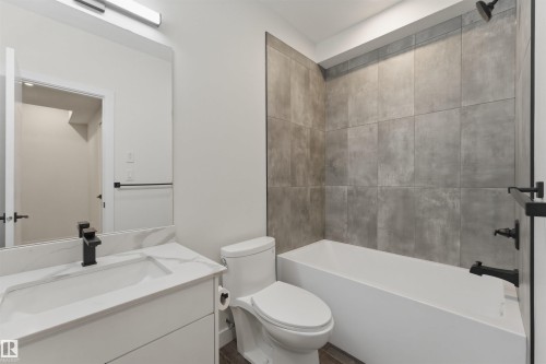 Bathroom featuring a white vanity with an integrated sink, black hardware, an illuminated mirror, a toilet, and a tiled shower-tub combination - 12447 47 Street, Edmonton, AB - Indoor Photo Showing Bathroom