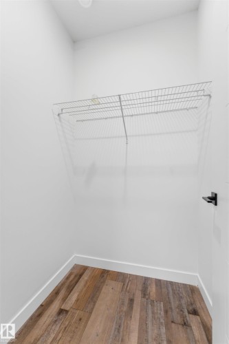 Walk-in closet featuring wood-finish flooring, white baseboards, white walls, wire shelving, and a black door handle - 12447 47 Street, Edmonton, AB - Indoor With Storage