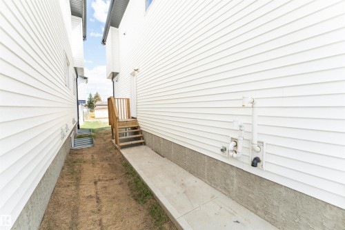Exterior side passage featuring white horizontal siding, a light wood staircase leading to a rear entrance, and a concrete pathway - 12447 47 Street, Edmonton, AB - Outdoor With Exterior