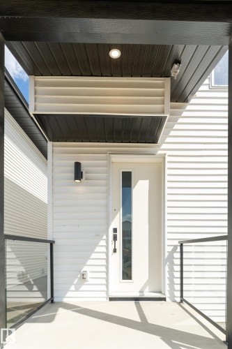 Contemporary entryway featuring a white vertical-paneled door with a full-length glass insert, a black wall-mounted sconce, and a recessed ceiling light - 12447 47 Street, Edmonton, AB -  With Exterior