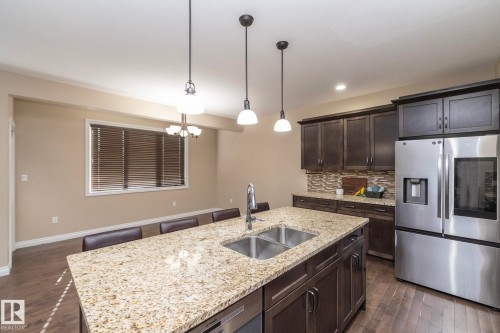 Spacious kitchen featuring a large island with a double stainless steel sink and granite countertop, dark wood cabinetry, a mosaic tile backsplash, and stainless steel appliances - 151 Caledonia Drive, Leduc, AB - Indoor Photo Showing Kitchen With Double Sink With Upgraded Kitchen