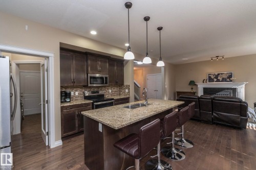 Open-concept kitchen with dark wood-finish cabinetry, stainless steel appliances, and a mosaic tile backsplash - 151 Caledonia Drive, Leduc, AB - Indoor Photo Showing Kitchen With Double Sink With Upgraded Kitchen