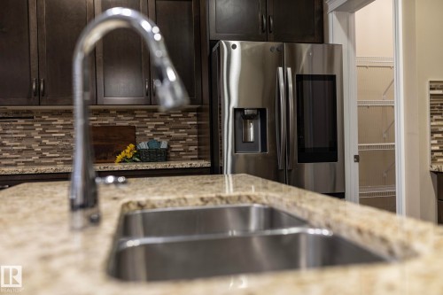 Kitchen featuring a double basin stainless steel sink with a chrome pull-down faucet, granite countertops, and dark wood cabinetry - 151 Caledonia Drive, Leduc, AB - Indoor Photo Showing Kitchen With Double Sink