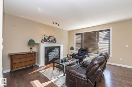 Living area featuring dark wood-finish flooring, a white mantel fireplace with a dark surround, and track lighting - 151 Caledonia Drive, Leduc, AB - Indoor Photo Showing Living Room With Fireplace