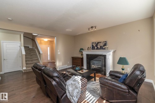 Living area featuring a white mantel fireplace with a black grate, wood-finish flooring, and light beige wall tones - 151 Caledonia Drive, Leduc, AB - Indoor Photo Showing Living Room With Fireplace
