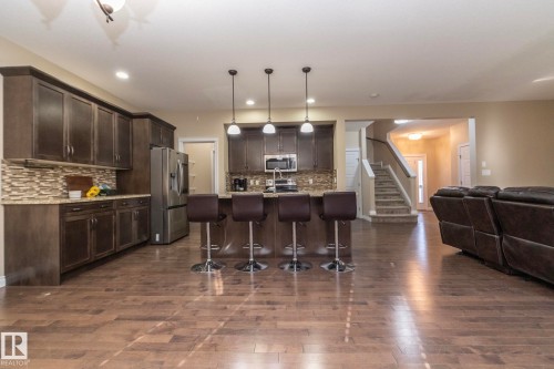Open-concept living area featuring rich wood-finish flooring, a kitchen island with pendant lighting, stainless steel appliances, and a tiled backsplash - 151 Caledonia Drive, Leduc, AB - Indoor Photo Showing Kitchen With Upgraded Kitchen