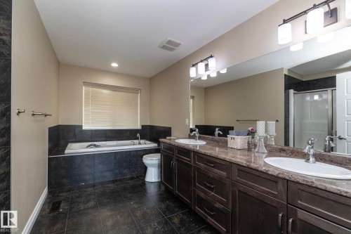 Bathroom featuring a double vanity with integrated sinks, a built-in soaking tub, a separate shower enclosure, dark wood-finish cabinetry, and tiled flooring - 151 Caledonia Drive, Leduc, AB - Indoor Photo Showing Bathroom
