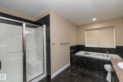 Bathroom featuring a glass-enclosed shower, a built-in tub with tile surround, dark tile flooring, and a window with blinds - 151 Caledonia Drive, Leduc, AB - Indoor Photo Showing Bathroom