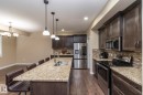Kitchen featuring an extended island with a double basin sink, stainless steel appliances, dark wood-finish cabinetry, and granite countertops - 151 Caledonia Drive, Leduc, AB  - Indoor Photo Showing Kitchen With Double Sink With Upgraded Kitchen 