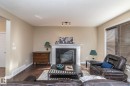 Living area featuring a fireplace with a black surround and white mantel, track lighting, wood-finish flooring, and a large window with blinds - 151 Caledonia Drive, Leduc, AB  - Indoor Photo Showing Living Room With Fireplace 