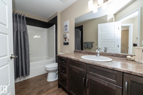 Bathroom featuring a dark wood-finish vanity with a single basin sink, a large wall-mounted mirror, and a full bathtub with a shower surround - 151 Caledonia Drive, Leduc, AB - Indoor Photo Showing Bathroom