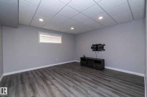 Spacious room featuring wood-finish flooring, a drop ceiling with recessed lighting, and a single window with blinds - 151 Caledonia Drive, Leduc, AB - Indoor