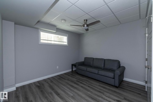 Spacious room featuring wood-finish flooring, a drop ceiling, and a ceiling fan with integrated lighting - 151 Caledonia Drive, Leduc, AB - Indoor