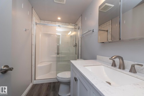 Bathroom featuring a glass-enclosed shower with subway tile surround, white vanity with integrated sink and stone-finish countertop, brushed nickel faucet, and wood-finish flooring - 151 Caledonia Drive, Leduc, AB - Indoor Photo Showing Bathroom