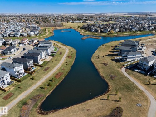 Aerial perspective showcasing a residential community with multiple homes bordering a central lake feature - 151 Caledonia Drive, Leduc, AB - Outdoor With Body Of Water With View