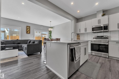 Modern kitchen featuring a central island with a sink, stainless steel appliances, white cabinetry, and wood-finish flooring - 319 36 Avenue, Edmonton, AB - Indoor Photo Showing Kitchen With Stainless Steel Kitchen With Upgraded Kitchen