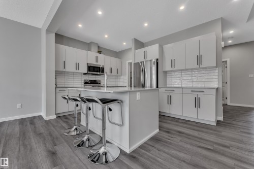 Modern kitchen featuring a central island, white cabinetry, stainless steel appliances, and wood-finish flooring - 319 36 Avenue, Edmonton, AB - Indoor Photo Showing Kitchen With Upgraded Kitchen