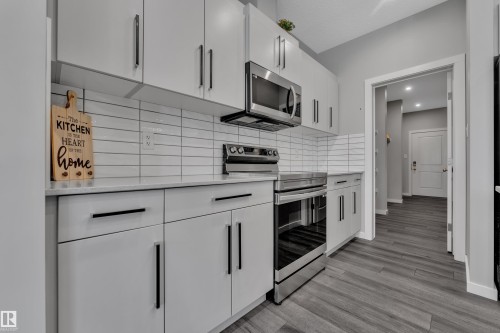 Contemporary kitchen featuring white cabinetry with black hardware, stainless steel appliances, a white subway tile backsplash, and light-toned countertops - 319 36 Avenue, Edmonton, AB - Indoor Photo Showing Kitchen With Upgraded Kitchen