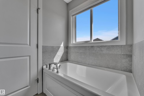 Built-in soaking tub with chrome fixtures, surrounded by grey tile wainscoting and light grey walls - 319 36 Avenue, Edmonton, AB - Indoor Photo Showing Bathroom