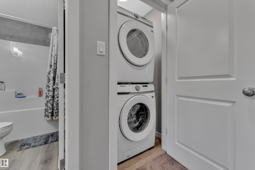 Stackable laundry appliances within a dedicated utility alcove, featuring a paneled interior door and light wood-finish flooring - 319 36 Avenue, Edmonton, AB - Indoor Photo Showing Laundry Room