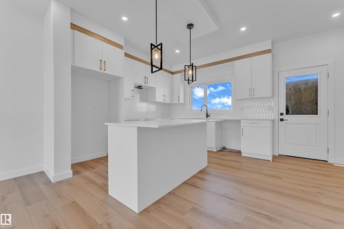 Modern kitchen featuring an island, white cabinetry with gold-tone hardware, wood-finish flooring, a white subway tile backsplash, and contemporary pendant lighting - 173 Graybriar Drive, Stony Plain, AB - Indoor Photo Showing Kitchen With Upgraded Kitchen