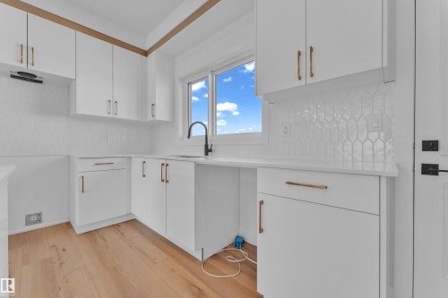 White cabinetry with gold-finish hardware, light wood-finish flooring, white geometric tile backsplash, white countertops, and a black gooseneck faucet - 173 Graybriar Drive, Stony Plain, AB - Indoor Photo Showing Kitchen
