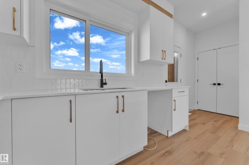 Kitchen workspace featuring a rectangular window, white cabinetry with gold-tone hardware, a single basin sink with a matte black faucet, and wood-finish flooring - 173 Graybriar Drive, Stony Plain, AB - Indoor Photo Showing Other Room