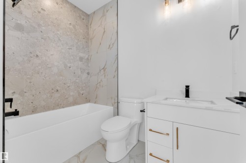 Contemporary bathroom featuring a white soaking tub with matte black fixtures, a tiled shower surround with varied stone-look panels, a white vanity with gold-tone hardware, a rectangular undermount sink, and a quartz countertop - 173 Graybriar Drive, Stony Plain, AB - Indoor Photo Showing Bathroom