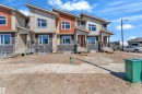 Modern townhome exterior featuring an asymmetrical roofline, stone veneer accents, and vibrant orange entry doors - 173 Graybriar Drive, Stony Plain, AB  - Outdoor With Facade 