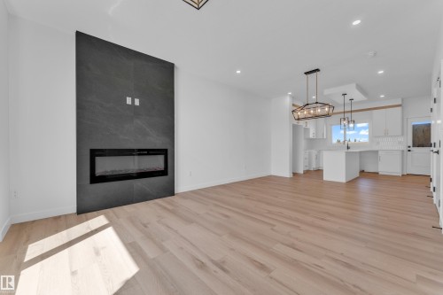 Open-concept living space featuring a floor-to-ceiling dark textured fireplace, electric insert, wood-finish flooring, recessed lighting, and modern light fixtures - 173 Graybriar Drive, Stony Plain, AB - Indoor Photo Showing Living Room With Fireplace