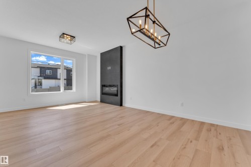 Spacious room featuring wood-finish flooring, a modern fireplace with a dark surround, and a large window - 173 Graybriar Drive, Stony Plain, AB - Indoor Photo Showing Other Room