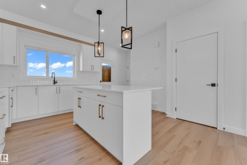 Modern kitchen featuring a central island with a white countertop and brass hardware, white cabinetry, wood-finish flooring, and two contemporary pendant lights - 173 Graybriar Drive, Stony Plain, AB - Indoor Photo Showing Kitchen