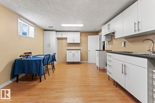 Kitchen area featuring white cabinetry, dark countertops, a double basin sink, and wood-finish flooring - 4908 59 Street, Cold Lake, AB - Indoor