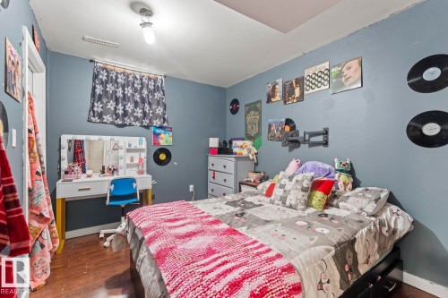 Room featuring wood-finish flooring, a wall-mounted light fixture, and a built-in window with patterned curtains - 4908 59 Street, Cold Lake, AB - Indoor Photo Showing Bedroom