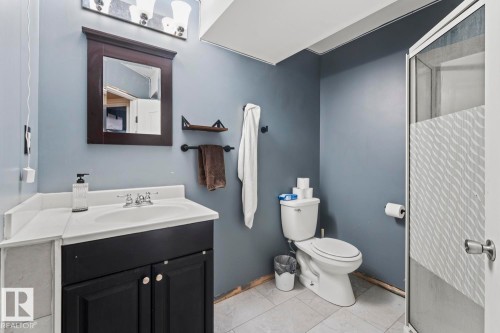 Full bathroom featuring a dark vanity with a white integrated sink, a dark framed mirror, white toilet, and a glass-enclosed shower with a patterned privacy film - 4908 59 Street, Cold Lake, AB - Indoor Photo Showing Bathroom