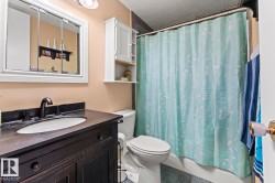 Bathroom featuring a dark wood vanity with an integrated sink and matte black faucet, a medicine cabinet, white wall-mounted storage, a toilet, and a shower-over-tub combination - 