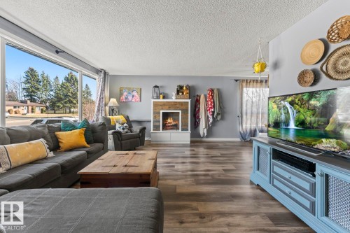 Spacious living area featuring large picture windows, wood-finish flooring, and a fireplace with a wood-paneled surround - 4908 59 Street, Cold Lake, AB - Indoor Photo Showing Living Room With Fireplace