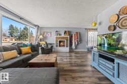 Spacious living area featuring large picture windows, wood-finish flooring, and a fireplace with a wood-paneled surround - 