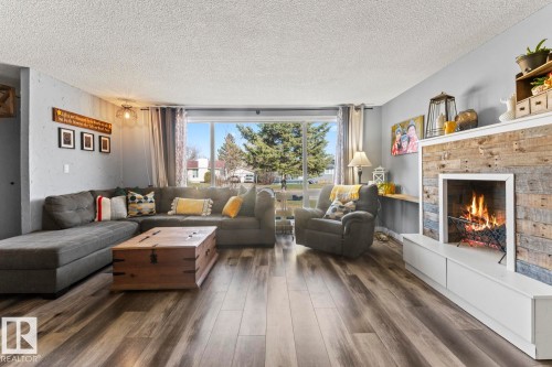 Spacious living area featuring wood-finish flooring, a rustic wood-paneled fireplace, and a large sliding glass door - 4908 59 Street, Cold Lake, AB - Indoor Photo Showing Living Room With Fireplace