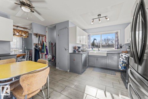 Kitchen featuring white upper cabinetry, gray lower cabinetry, a farmhouse sink, and a large window - 4908 59 Street, Cold Lake, AB - Indoor Photo Showing Other Room