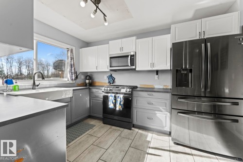 Kitchen featuring two-tone cabinetry, stainless steel appliances, a farmhouse sink with a black gooseneck faucet, and wood-finish tile flooring - 4908 59 Street, Cold Lake, AB - Indoor Photo Showing Kitchen With Upgraded Kitchen