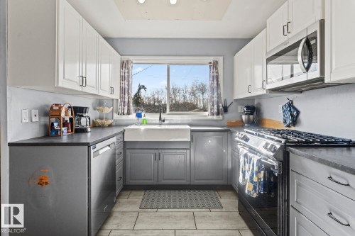 U-shaped kitchen featuring two-tone cabinetry, stainless steel appliances, a farmhouse sink, and tile flooring - 4908 59 Street, Cold Lake, AB - Indoor Photo Showing Other Room