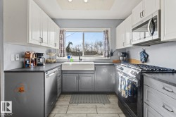 U-shaped kitchen featuring two-tone cabinetry, stainless steel appliances, a farmhouse sink, and tile flooring - 