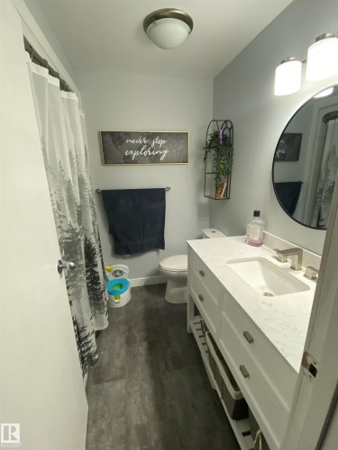 The bathroom features a vanity with a white countertop and an integrated sink, a toilet, and dark-toned flooring - 5030 40 Street, Cold Lake, AB - Indoor Photo Showing Bathroom