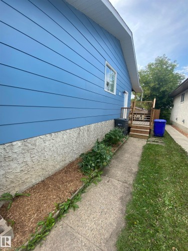 The property features blue siding, a wooden deck with stairs, and a garden bed with plants and wood chips - 5030 40 Street, Cold Lake, AB - Outdoor