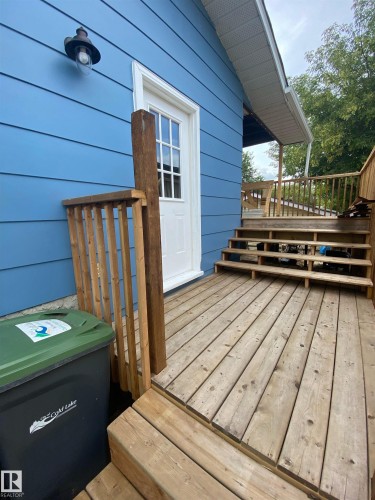 The property features a wooden deck with railing, a white exterior door with glass panes, and blue siding - 5030 40 Street, Cold Lake, AB - Outdoor With Exterior
