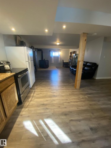 Open concept area featuring wood-look flooring, recessed lighting, and a kitchen area with wood cabinetry and stainless steel appliances - 5030 40 Street, Cold Lake, AB - Indoor